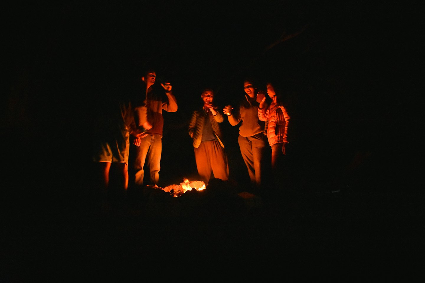 Young adults share stories around a warm campfire at night.